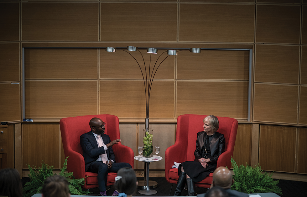A man and a woman seated in red chairs on a stage
