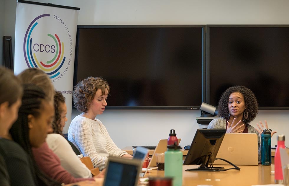 Woman at the head of a table speaking while others listen. Banner reading CDCS to the side.