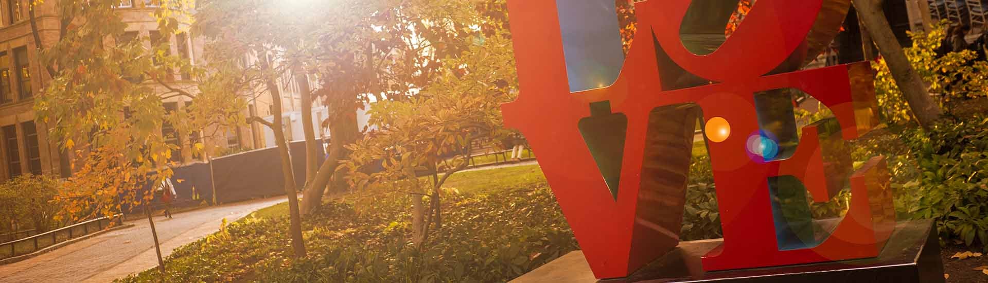 Love 1920 x 550.jpg View of trees and buildings on campus with LOVE statue in the foreground