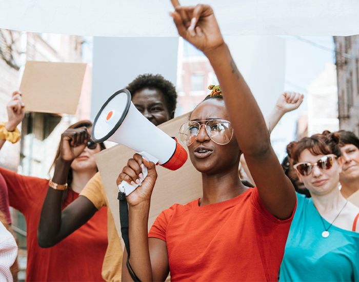 Woman in an orange shirt at protest with a megaphone, Photo Credit: Rawpixel on iStock