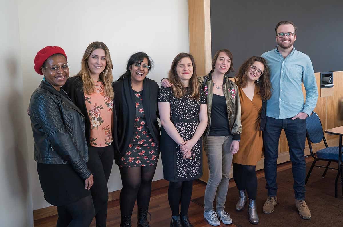 Seven people posing in a line, smiling