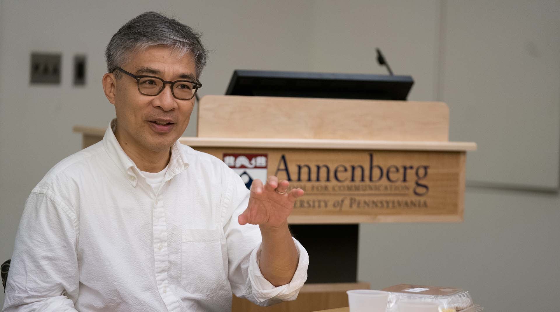 Guobin Yang seated at a table and speaking during a meeting