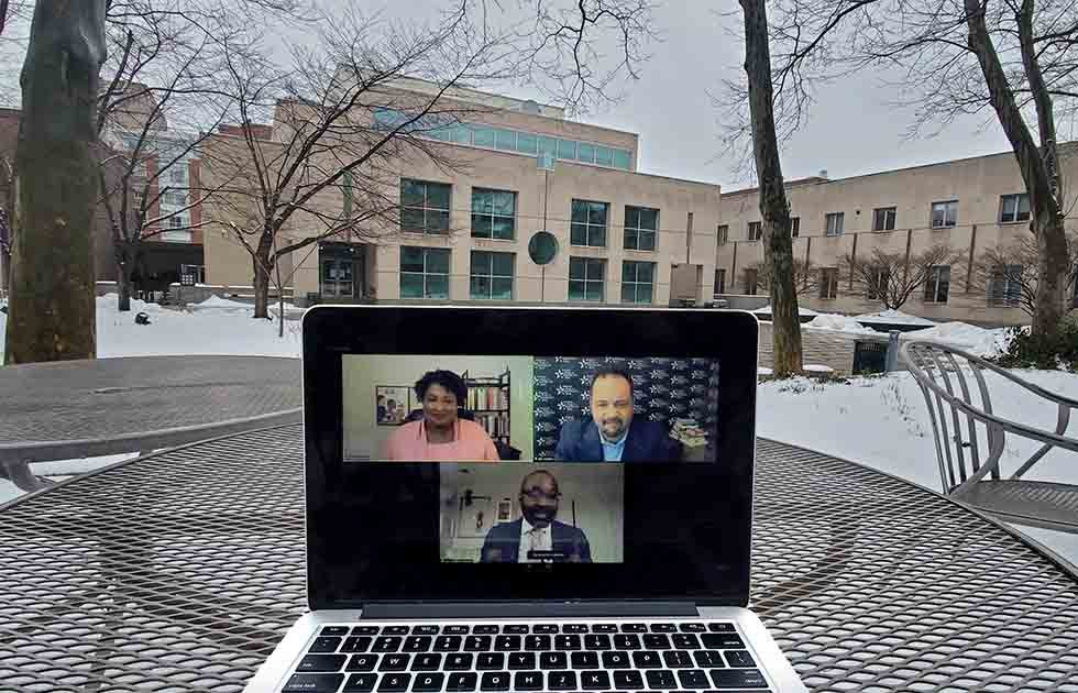 Laptop with the faces of Stacey Abrams, Ben Jealous, and John L. Jackson, Jr. on a table outside with the Annenberg building in the background