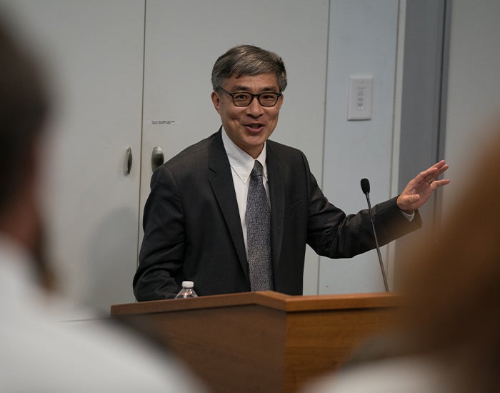 Guobin Yang, Ph.D., in a suit, speaking at a podium