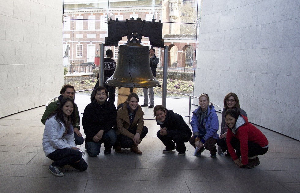 A group of people crouched down, surrounding a giant bell