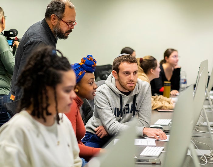 Three students and a professor looking at a computer screen (screen not visible)