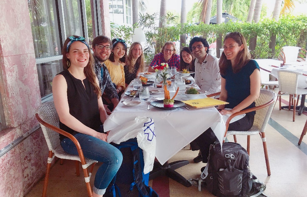 group of people having dinner together in Miami while the sun is out. They are all smiling for the picture.