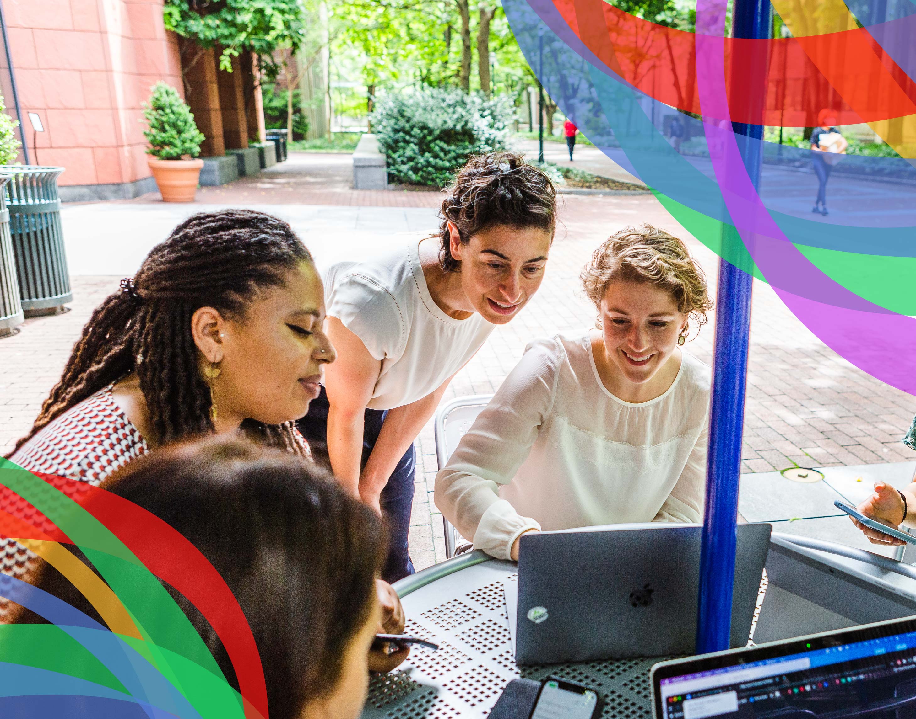 Four women happily working on laptops at an outdoor table