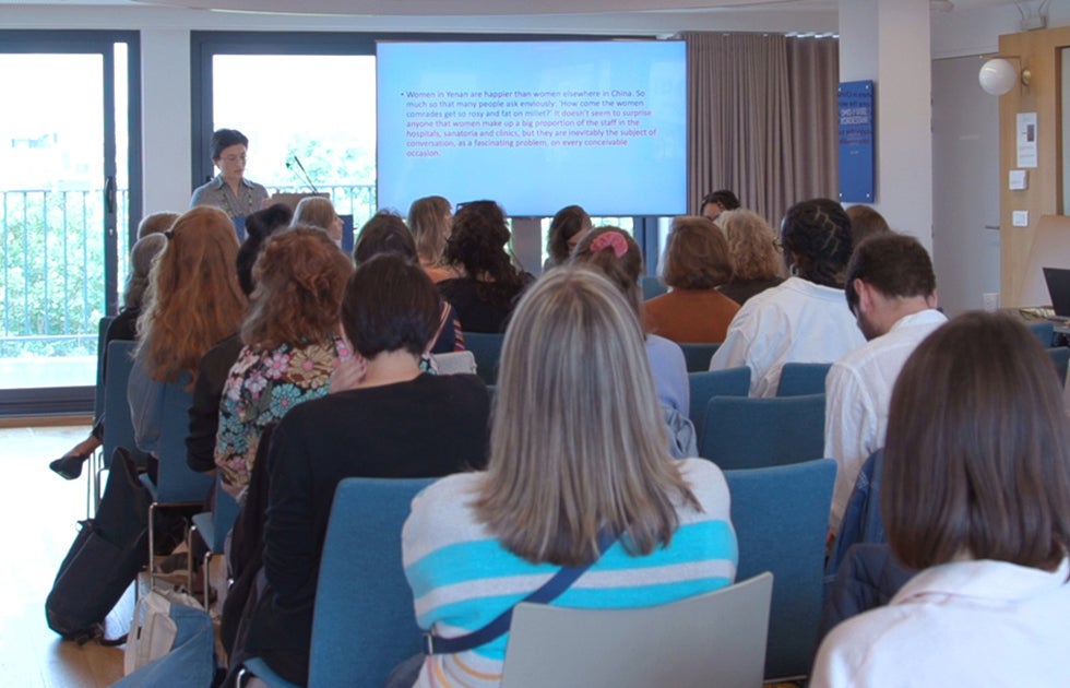 Seated audience listening to a female presenter speak from a podium