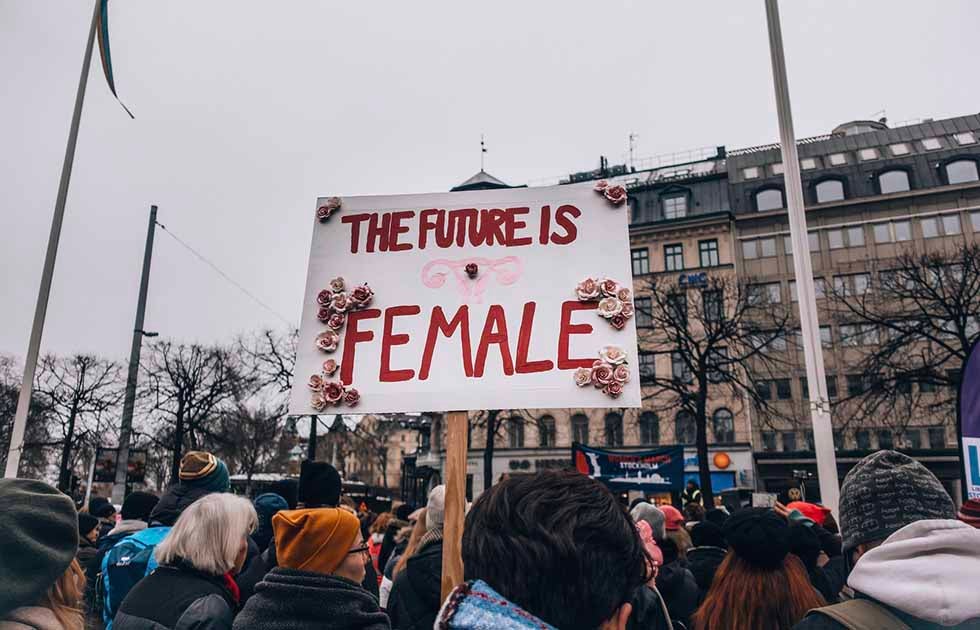 Protesters marching outdoors with a sign reading &quot;The Future is Female&quot;, Photo Credit: Lindsey Lamont / Unsplash