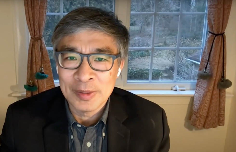 Guobin Yang speaking sitting in front of a window with curtains