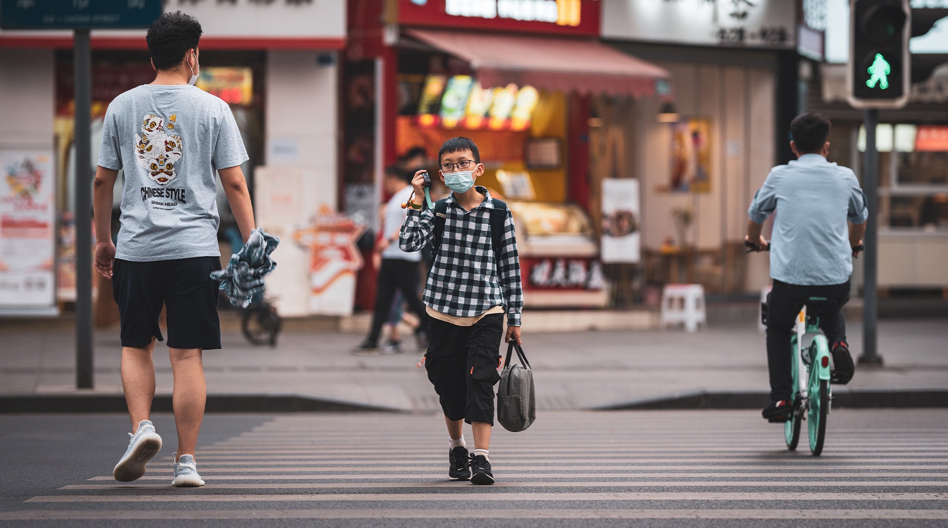 Three people walking in a crosswalk and wearing face masks. Li Lin on Unsplash.