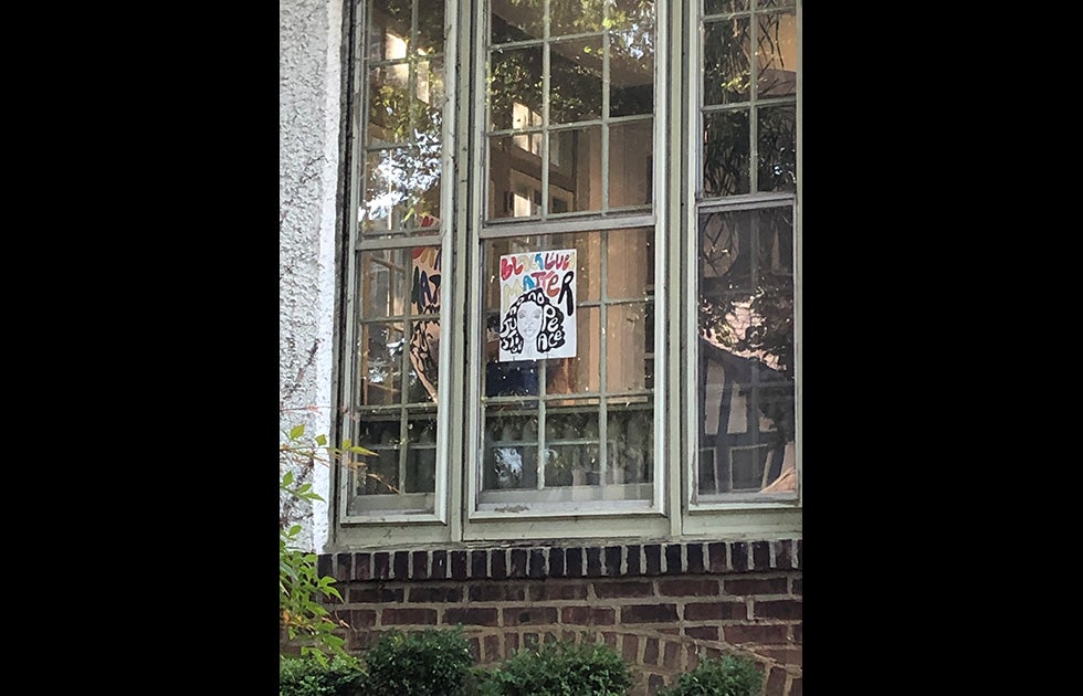 Window with a “Black Lives Matter” sign. The lettering is multicolored. There is also a hand-drawn portrait of a woman whose hair has letters in it reading “No Justice No Peace”