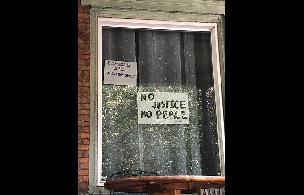 A window with two handmade signs. One says “No justice no peace #BLM” and is written in Black paint. Another appears to be written in different colors of markers and says “I shouldn’t be scared to be a Black teenager”