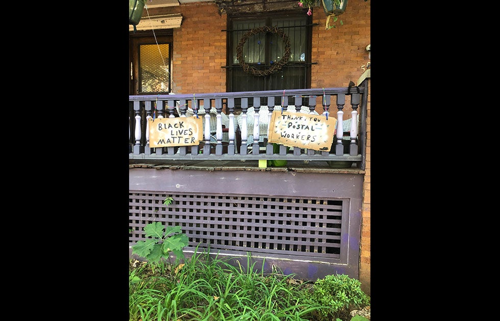 two signs made from cardboard boxes. One says “Black Lives Matter” and the other says “Thank you postal workers” with little hearts around it, both written in Black marker or paint.