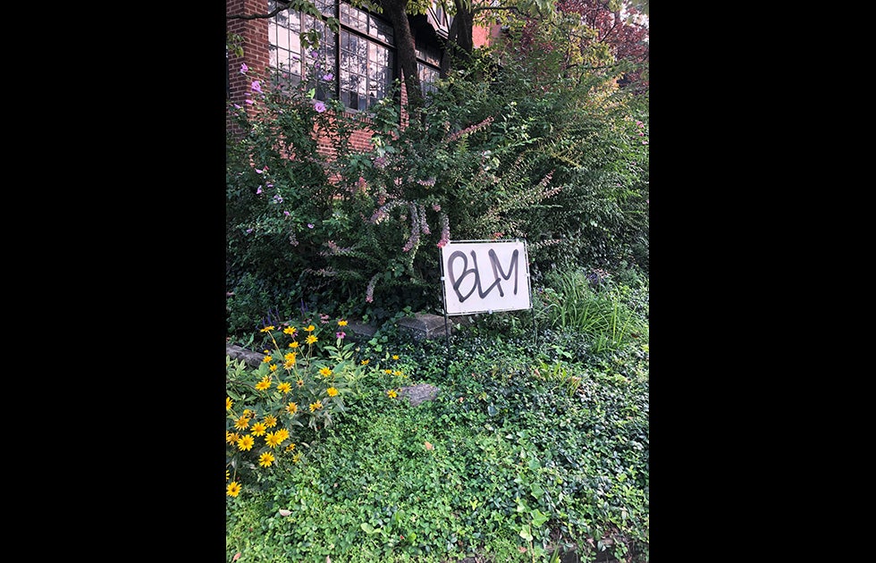 Handmade sign that says BLM amongst flowers, ivy, and weeds.