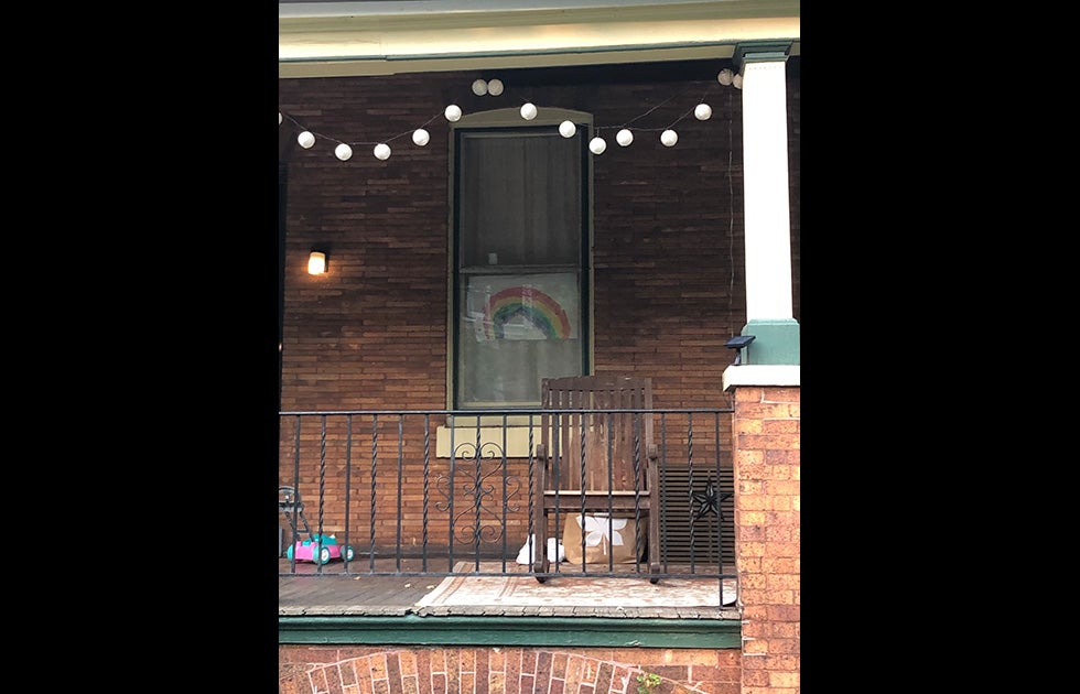 An apartment window with a hand painted rainbow. There is a child’s toy on the porch.