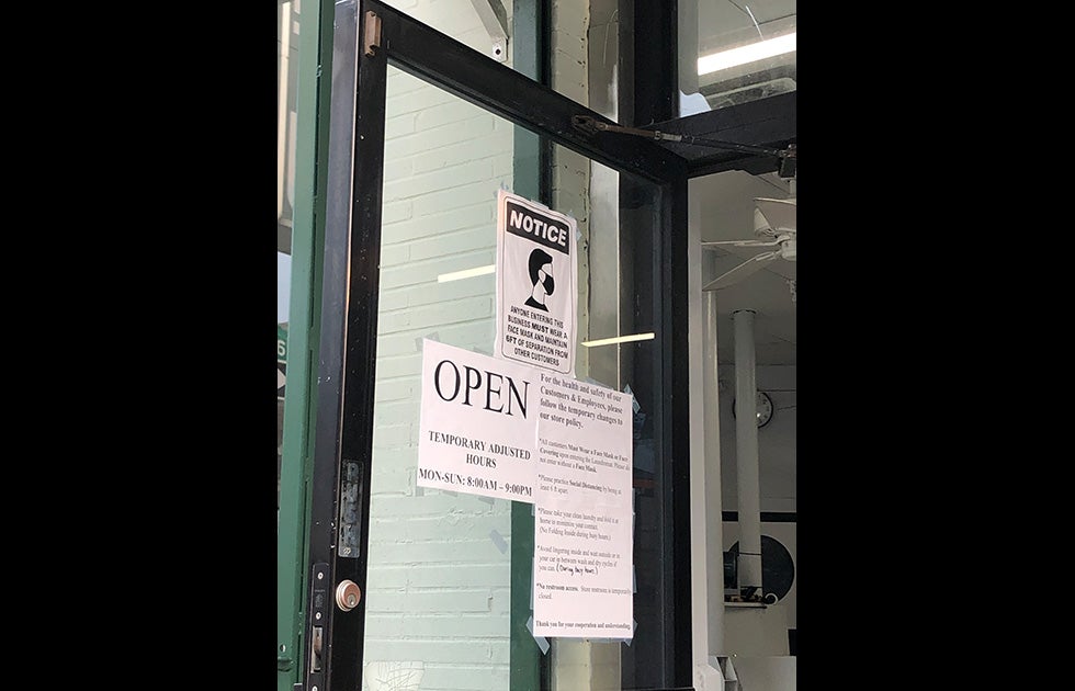 A laundromat door with various signs about temporary hours, changes to policy, and mask/distancing requirements.