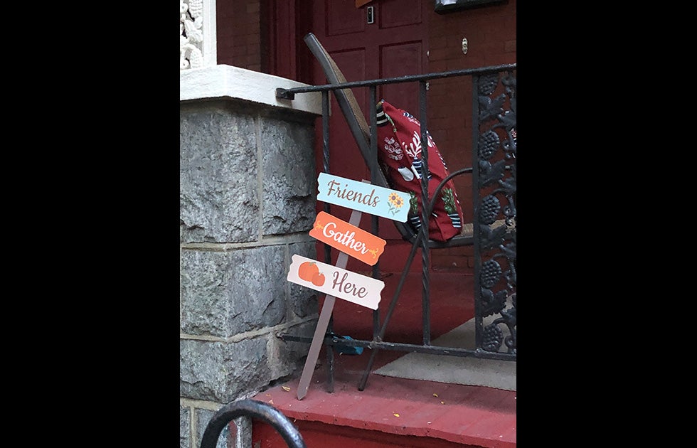 A Halloween/fall decoration that reads “Friends gather here” and is decorated with with flowers and pumpkins.
