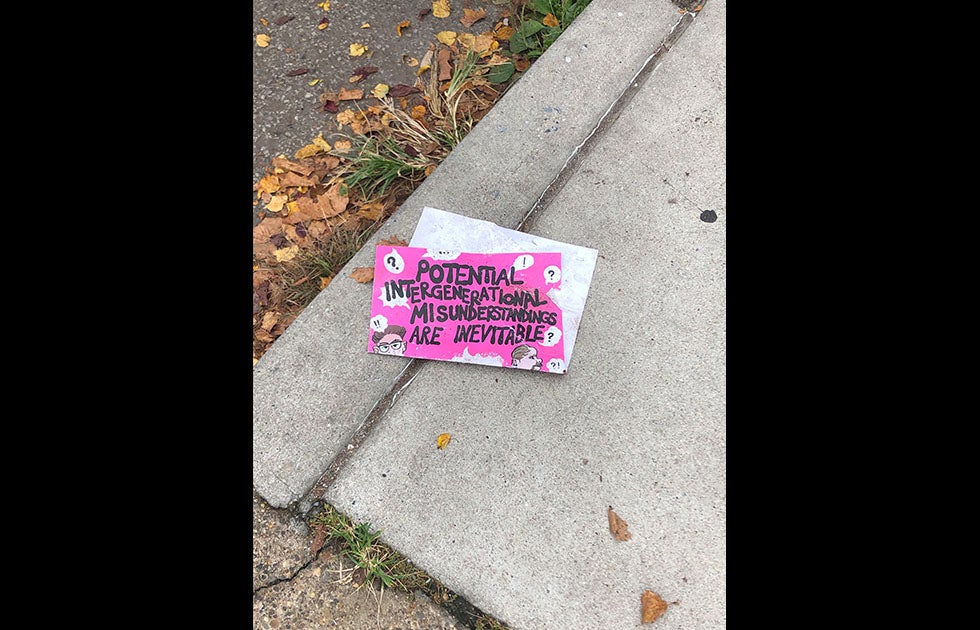 Sign on the ground that says “Potential intergenerational misunderstandings are inevitable” and two hand drawn white men. There are various thought bubbles with ? And ! In them.