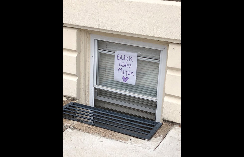 Handmade “Black Lives Matter” sign made in purple crayon with a heart. It is hung in a window low to the sidewalk.