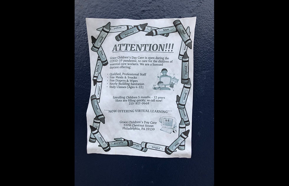 Sign on printer paper advertising daycare that is open during the Covid-19 pandemic with clip art of crayons of different colors (though printed in black and white/grayscale) with clip art of a smiling computer and 3 smiling kids next to a computer