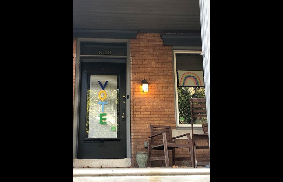 An apartment with the letters VOTE going downward on the door and a drawing of a rainbow (likely done by a child) in the window.