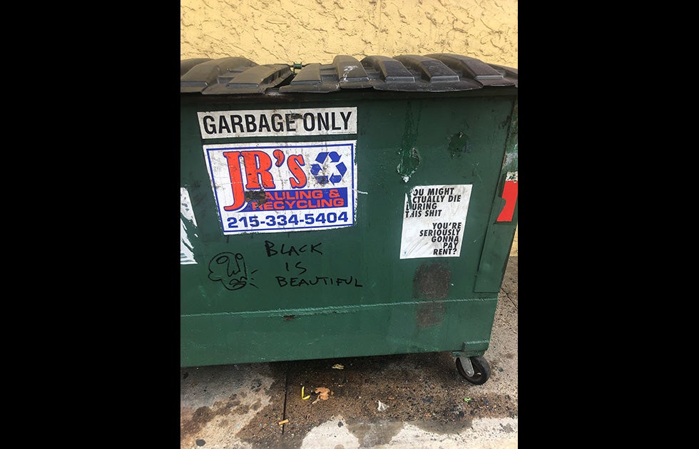 Dumpster with “Black is Beautiful” written in a Black marker with an abstract drawing of a face next to it. And an 8”x11” sign that appears to have been printed from a computer that is slightly torn and reads “You might actually die during this shit/You’re seriously gonna pay rent?”