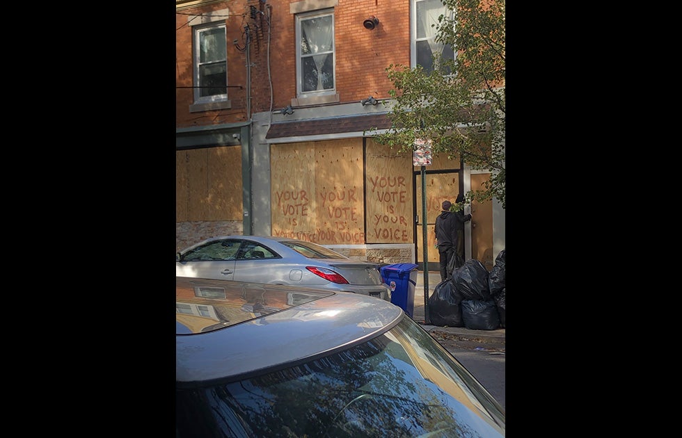 A business building with the windows boarded up and “Your vote is your voice” spray painted multiple times across it.  Note: The boards were likely put up in anticipation for violence and vandalization on election night and in the days after, as many businesses had concerns.
