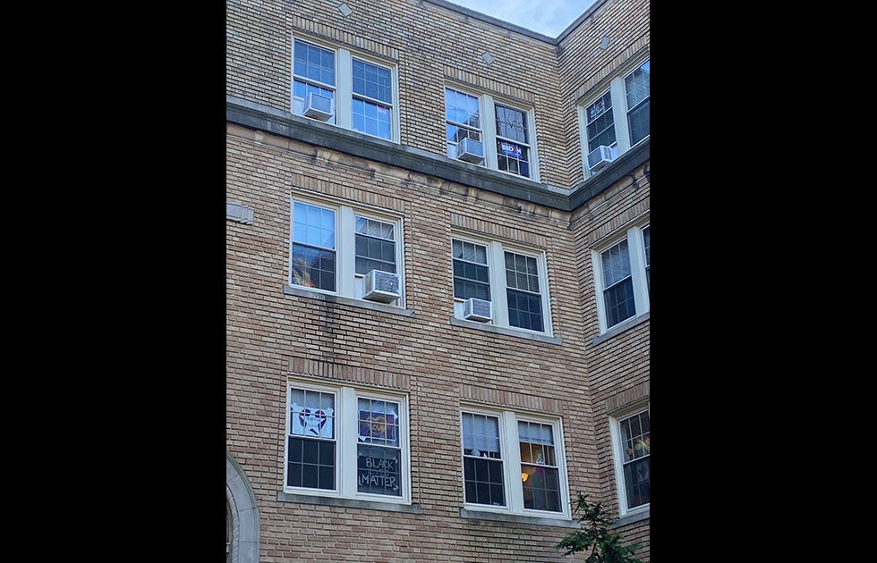 an apartment building with multiple windows with signs. Two say Black Lives Matter, one says Love, two say Biden Harris, and one says “I will vote 11.3.20”
