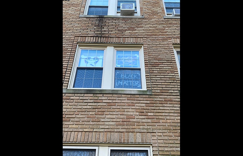 An apartment window with three signs. One is homemade and says “Black Lives Matter” and two are not handmade and say “I will vote 11.3.20” and “Love” in a heart.