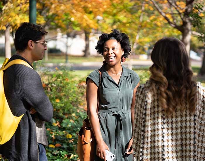 Sanjay Flo Devo 700 x 550.jpg Three students standing in a circle on a fall day outside. One is laughing.