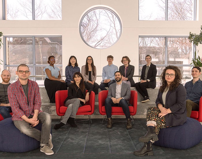 Two professors and ten students seated in a horseshoe shape with a wall of windows behind them