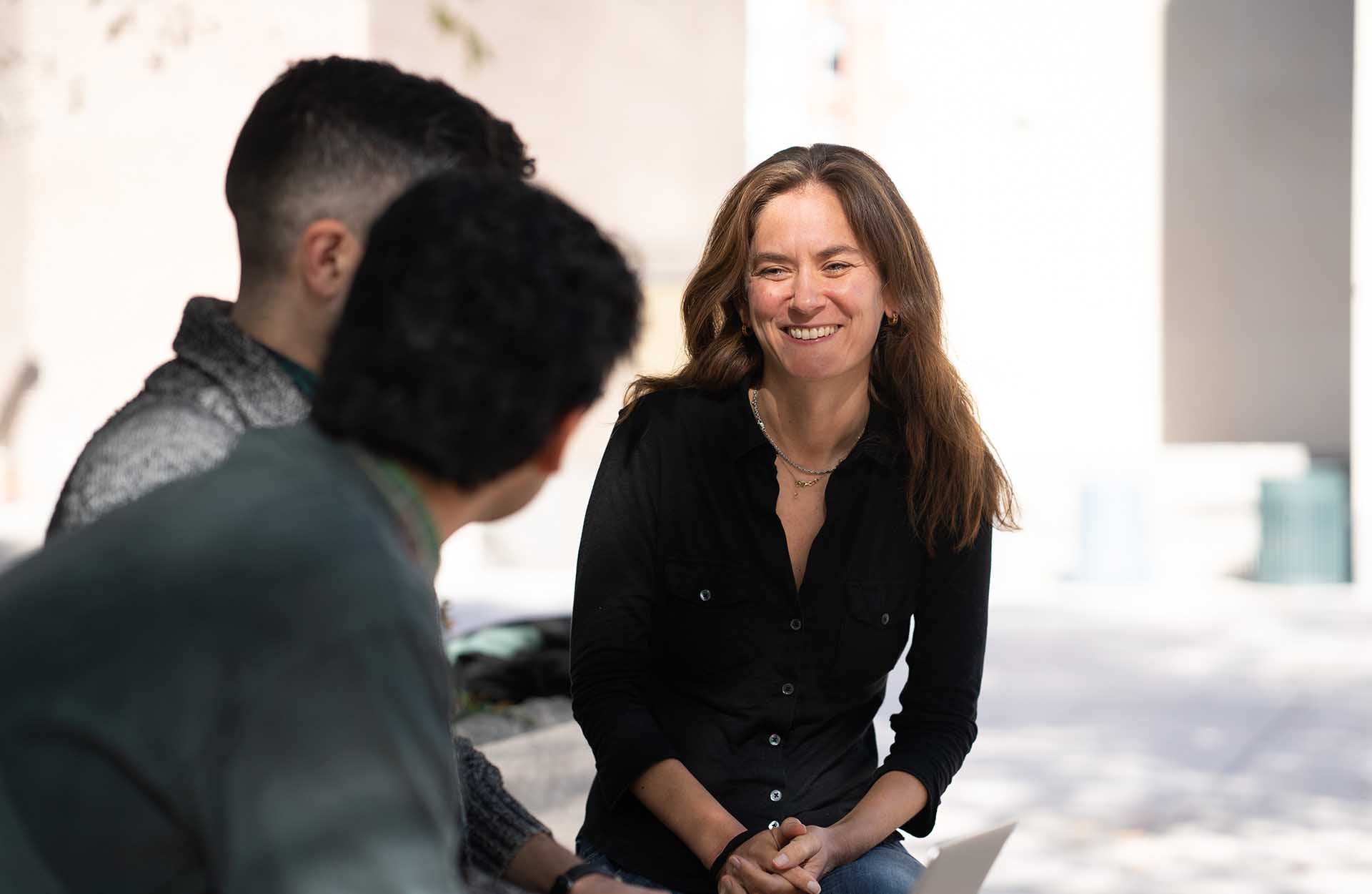 Emily Falk and Lab 1920 x 1250.jpg Emily Falk seated outside smiling at two people whose faces are unseen