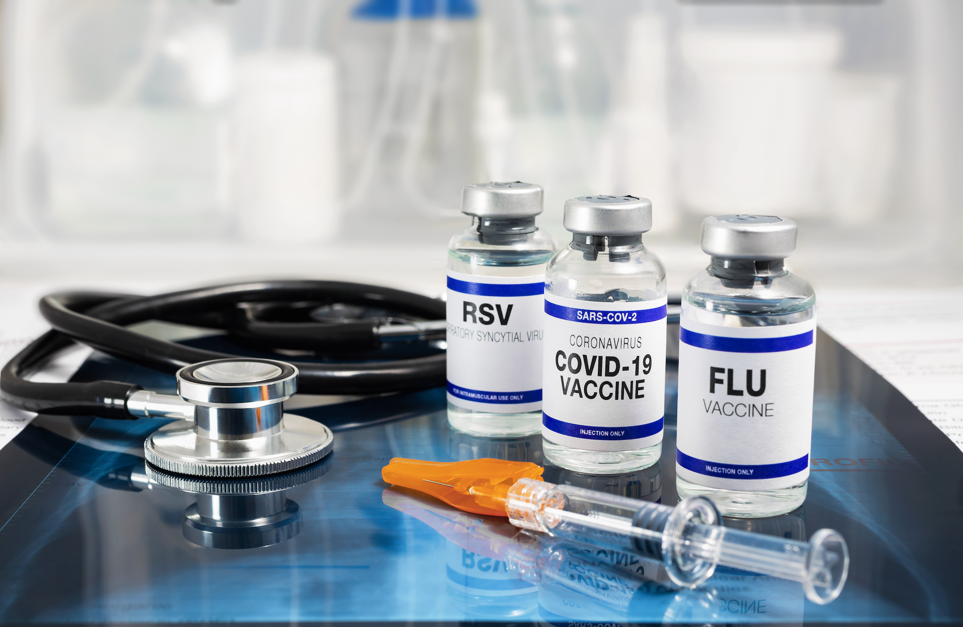 COVID-flu-RSV header.png Bottles of vaccine for Influenza Virus, Respiratory Syncytial virus and Covid-19 for vaccination. Flu, RSV and Sars-cov-2 Coronavirus vaccine vials over Radiography pulmonar with stethoscope