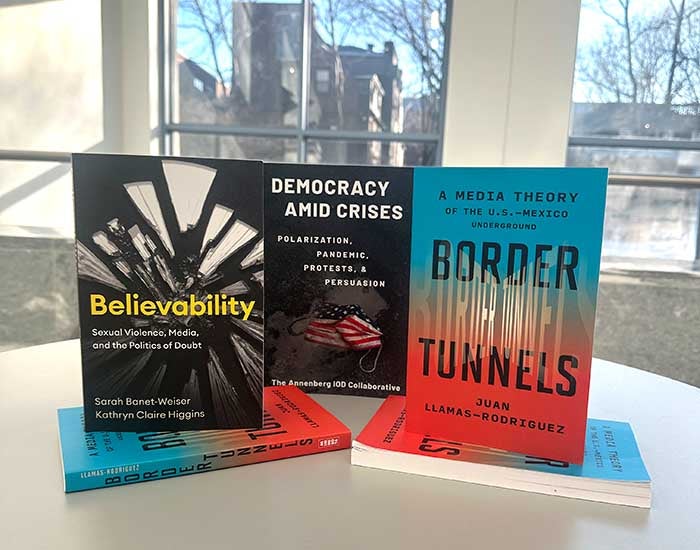Three books displayed on a table with windows behind