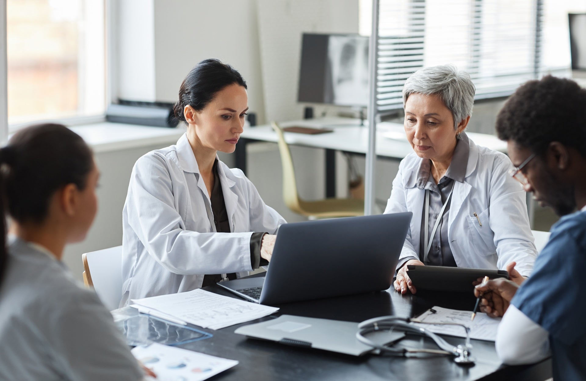 two doctors looking at a laptop next to two doctors sitting at a table