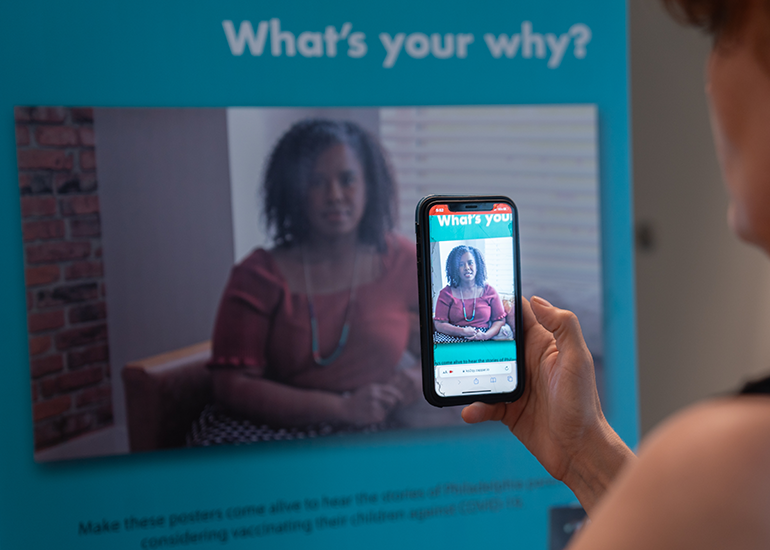 A person holds a phone up to a poster and watches an augmented reality experience.