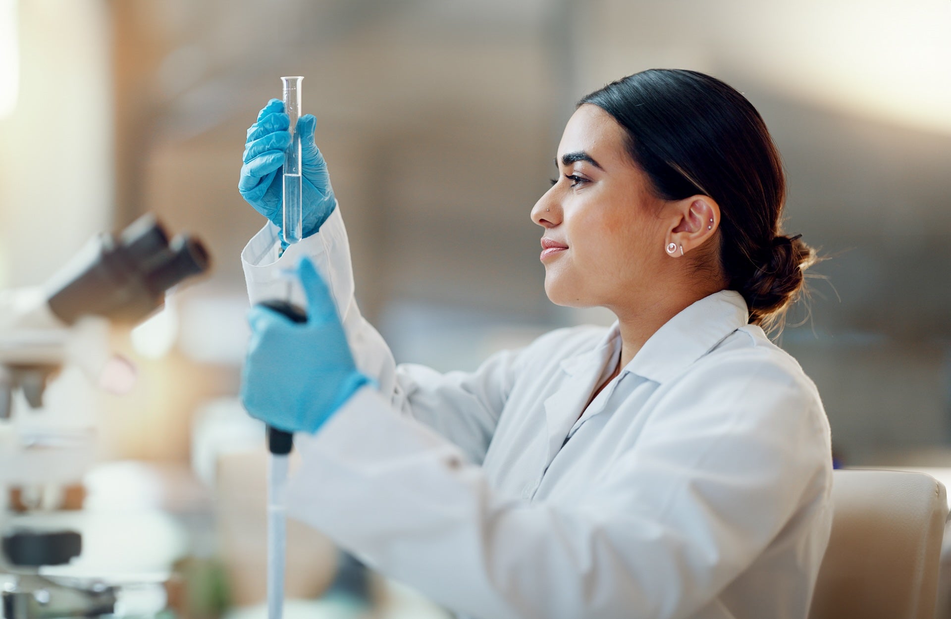 a doctor wearing a lab coat and gloves stands in a lab holding a pipette