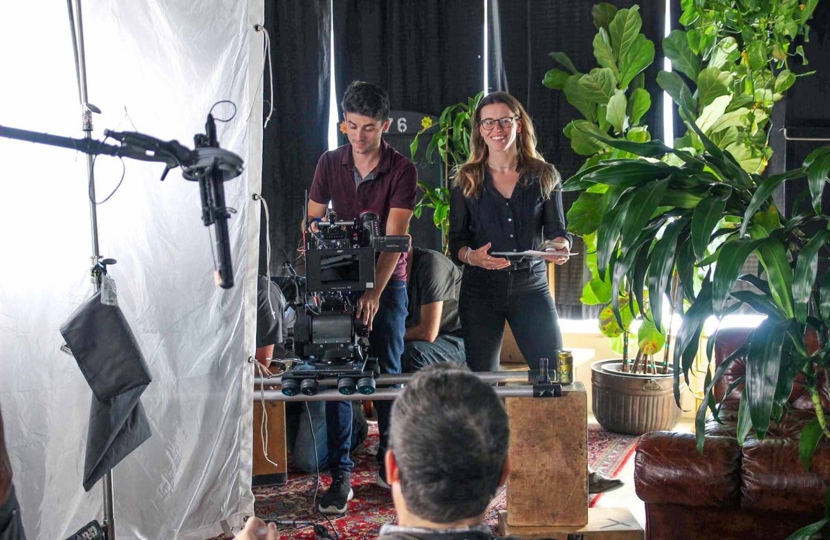 Katie Koeblitz on set directing with a man behind a camera, pointed at a person being interviewed