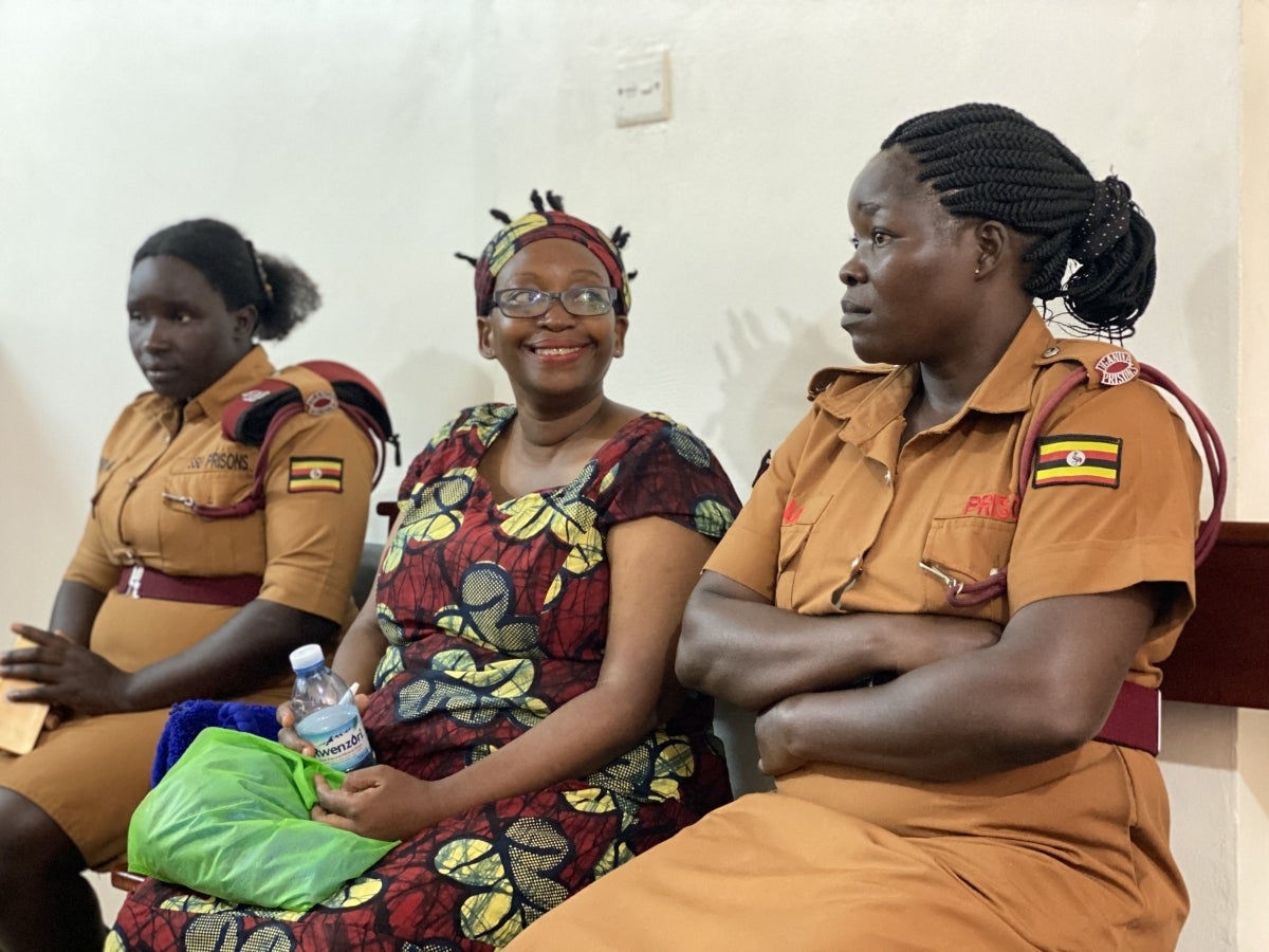 A Ugandan woman smiling and sitting between two female prison guards