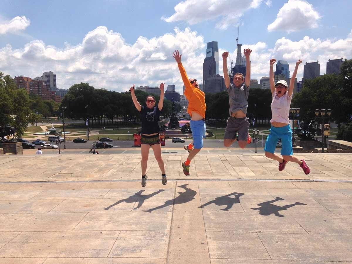 Four people jumping in mid-air with their arms up with the Philadelphia skyline in the background