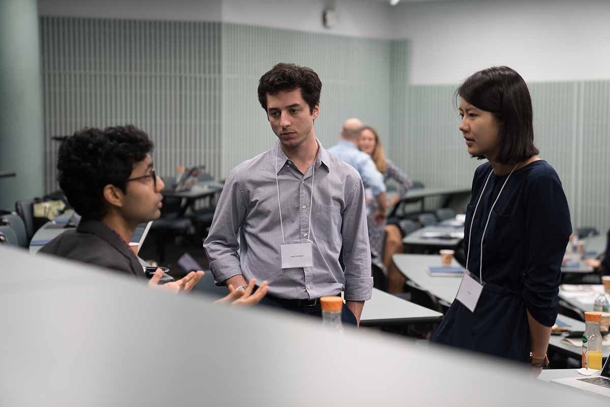 Three people standing in a triangle discussing something in a classroom