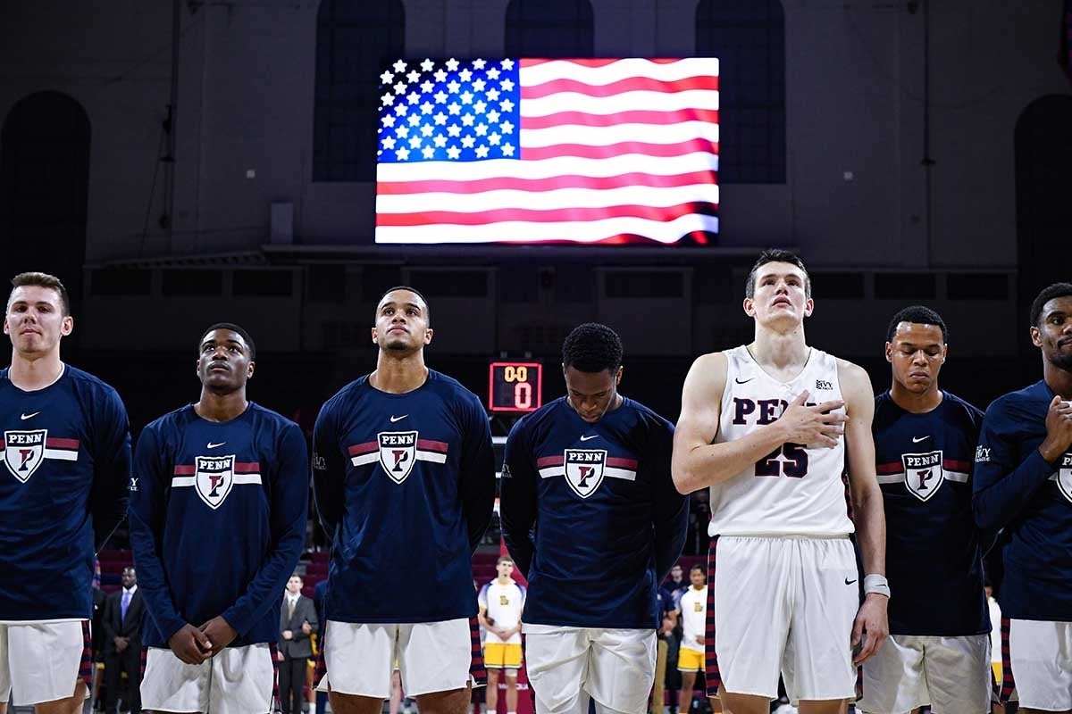 Penn athletes standing solemnly for the national anthem with a flag behind them