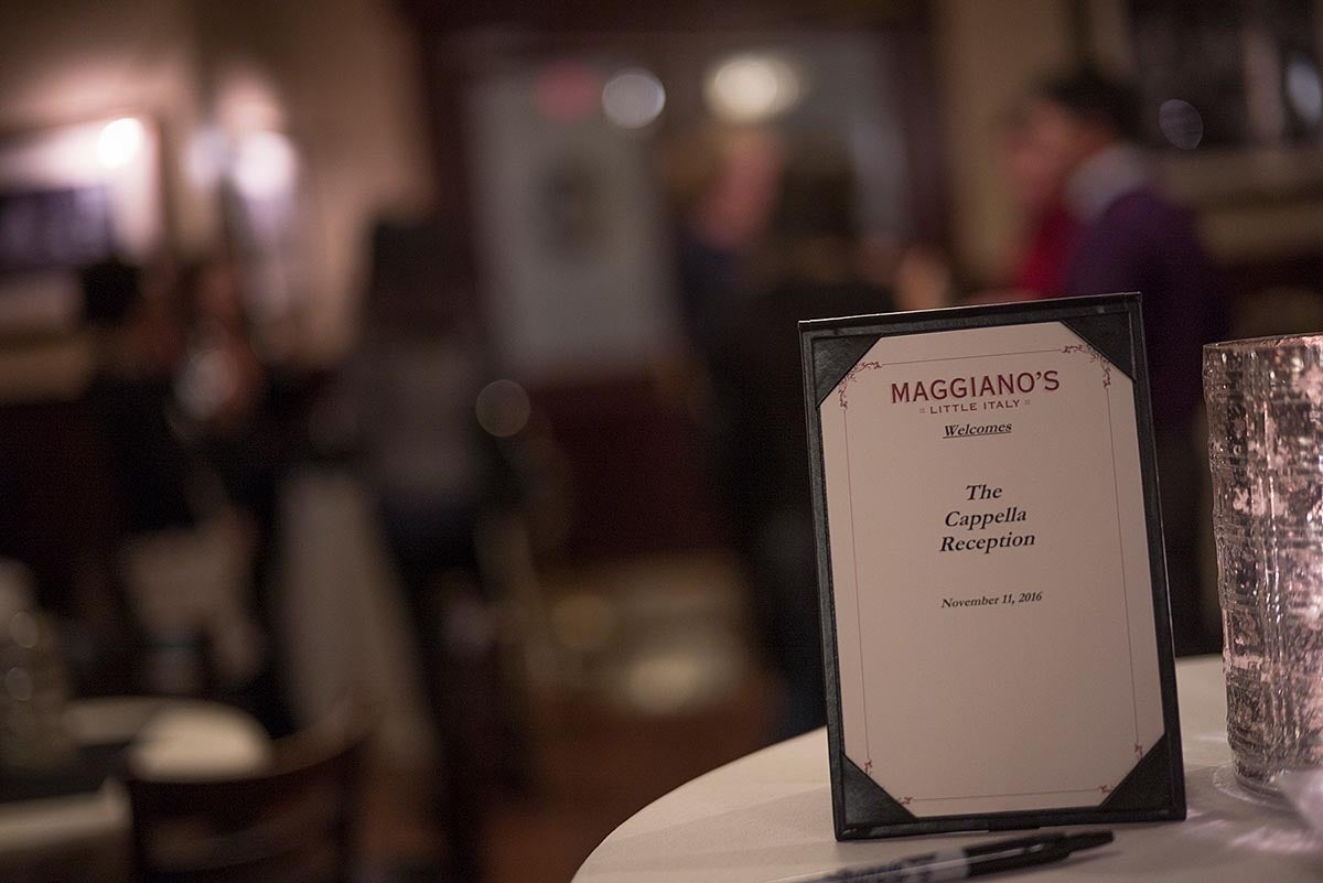 Close-up picture of a black menu-holder with a paper that says "Maggiano's Little Italy welcomes The Cappella Reception, November 11, 2016". The restaurant's new is in red text and the rest of the text is in black and italicized, with the word 'welcomes' being underlined.