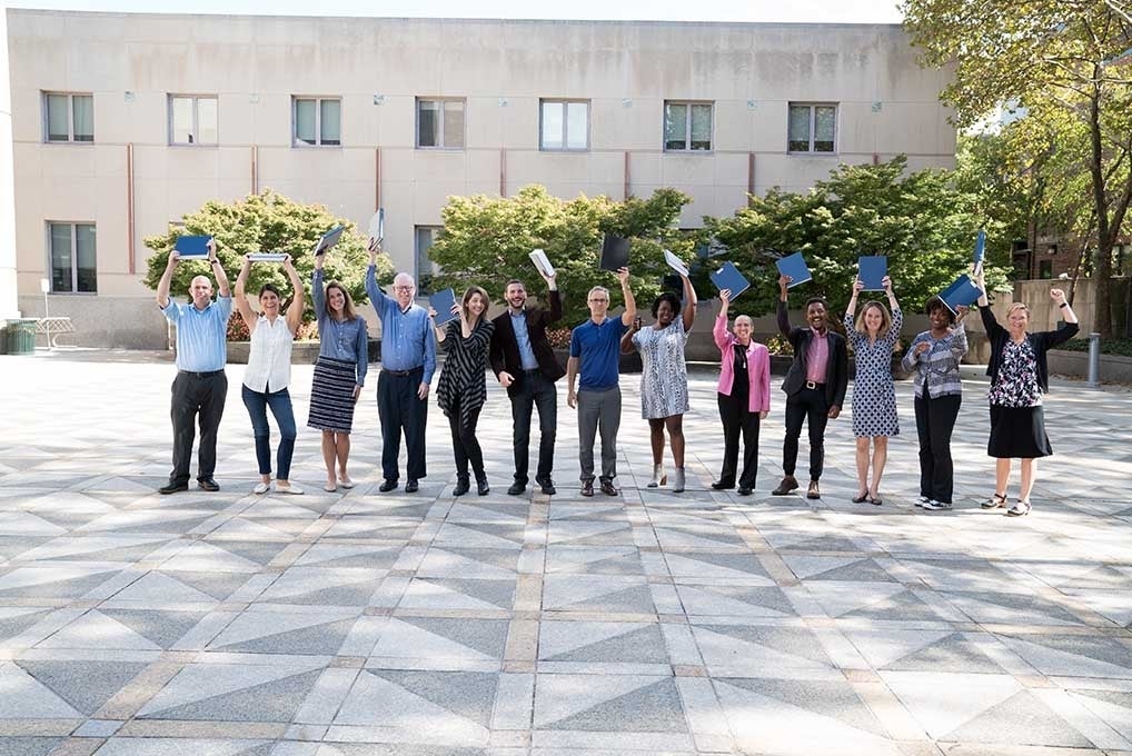 Presenters lined up and posing while holding up their dissertations