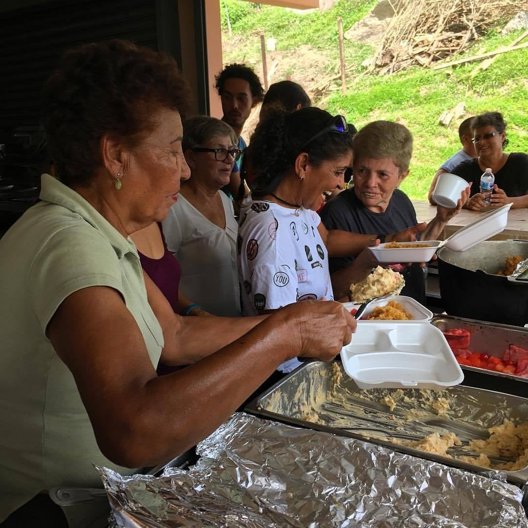 Volunteers behind a table serving food in styrofoam containers to those waiting.