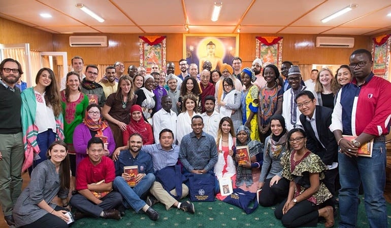 Group photo of the attendees of the event with Dalai Lama in the middle. The front row has been sitting and kneeling, the second row has people kneeling, and the other three rows are standing. 