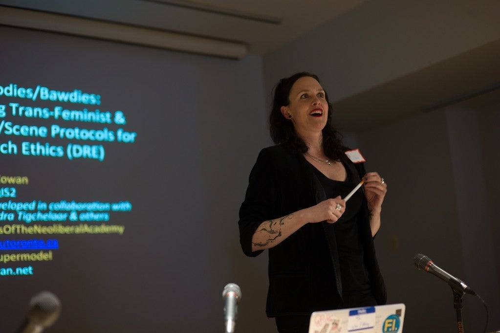 TL Cowan presenting "The Internet of Bodies/The Internet of Bawdies." The powerpoint is in the back as T.L. speaks to the audience 