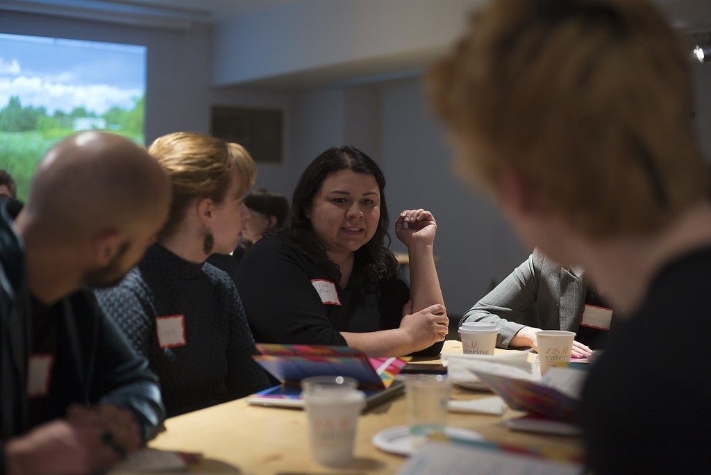 Rosemary Clark and Elena Maris engaged in group discussion with others at their light brown table where they are all seated. On the table, there are programs and coffee cups.